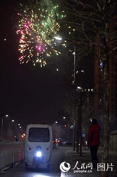 煙花在夜空中綻放，忙完一天工作的張宏鑫用手機拍下瞬間的美景。（人民網記者 翁奇羽 攝）